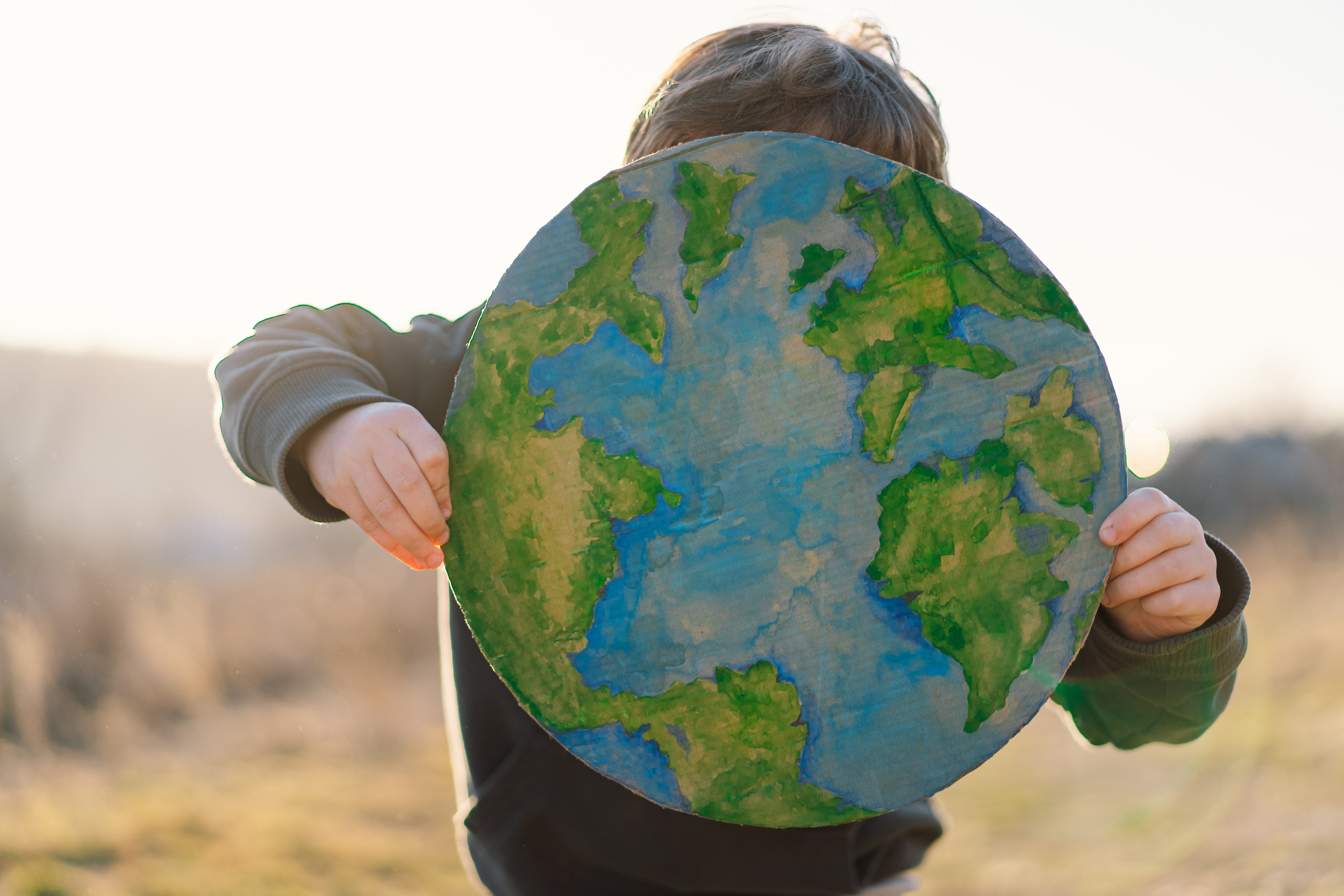 Little boy holding planet in hands against green spring background